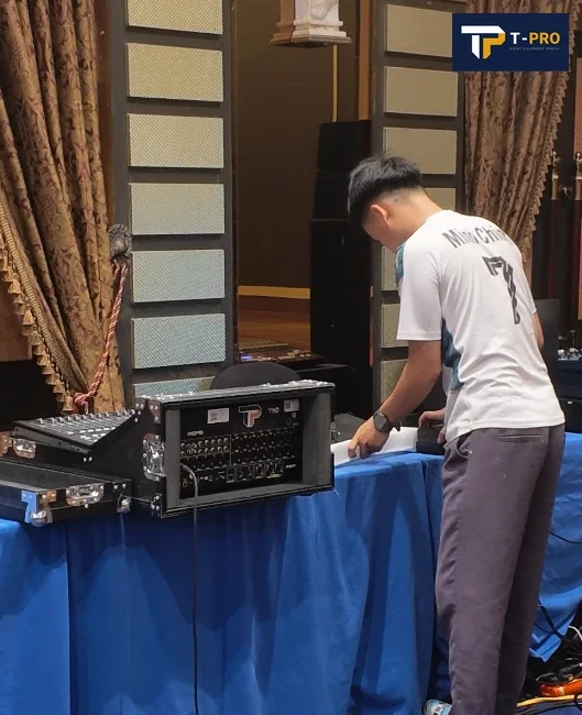 Nh&acirc;n sự đứng b&ecirc;n b&agrave;n phủ khăn xanh, cạnh rack thiết bị v&agrave; b&agrave;n điều khiển nhỏ.